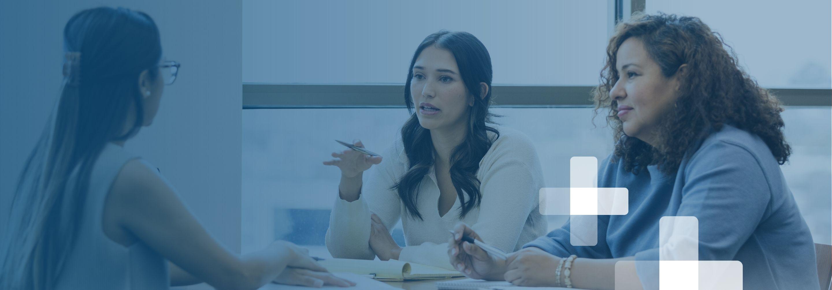 Three women in business casual clothing hold a professional meeting