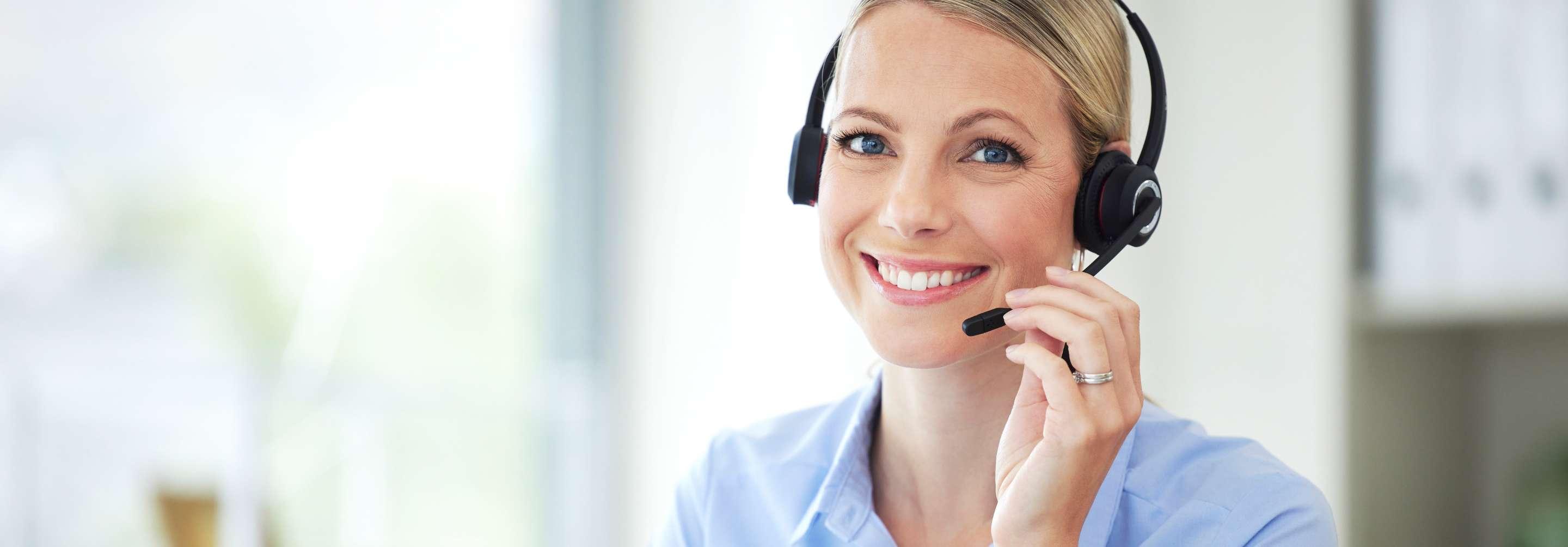 A claims researcher in a blue button-down shirt smiles into the camera, lightly touching her headset