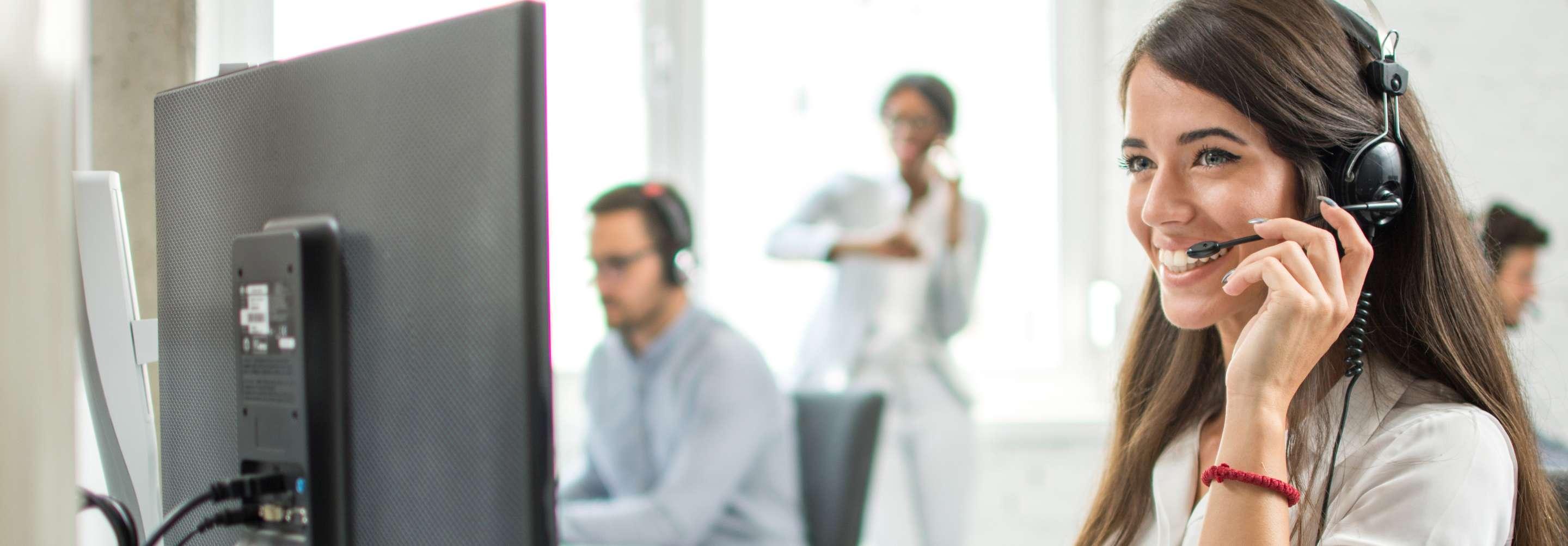 A credentialing specialist smiles as she speaks with someone over the phone, lightly touching her headset