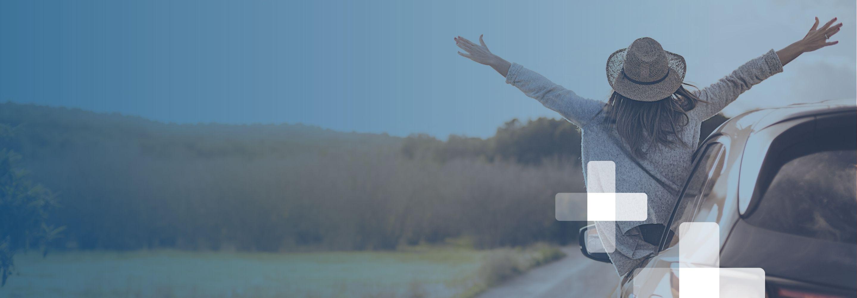 A woman leans out the drivers' side window of her stopped vehicle with arms flung wide, celebrating the view ahead
