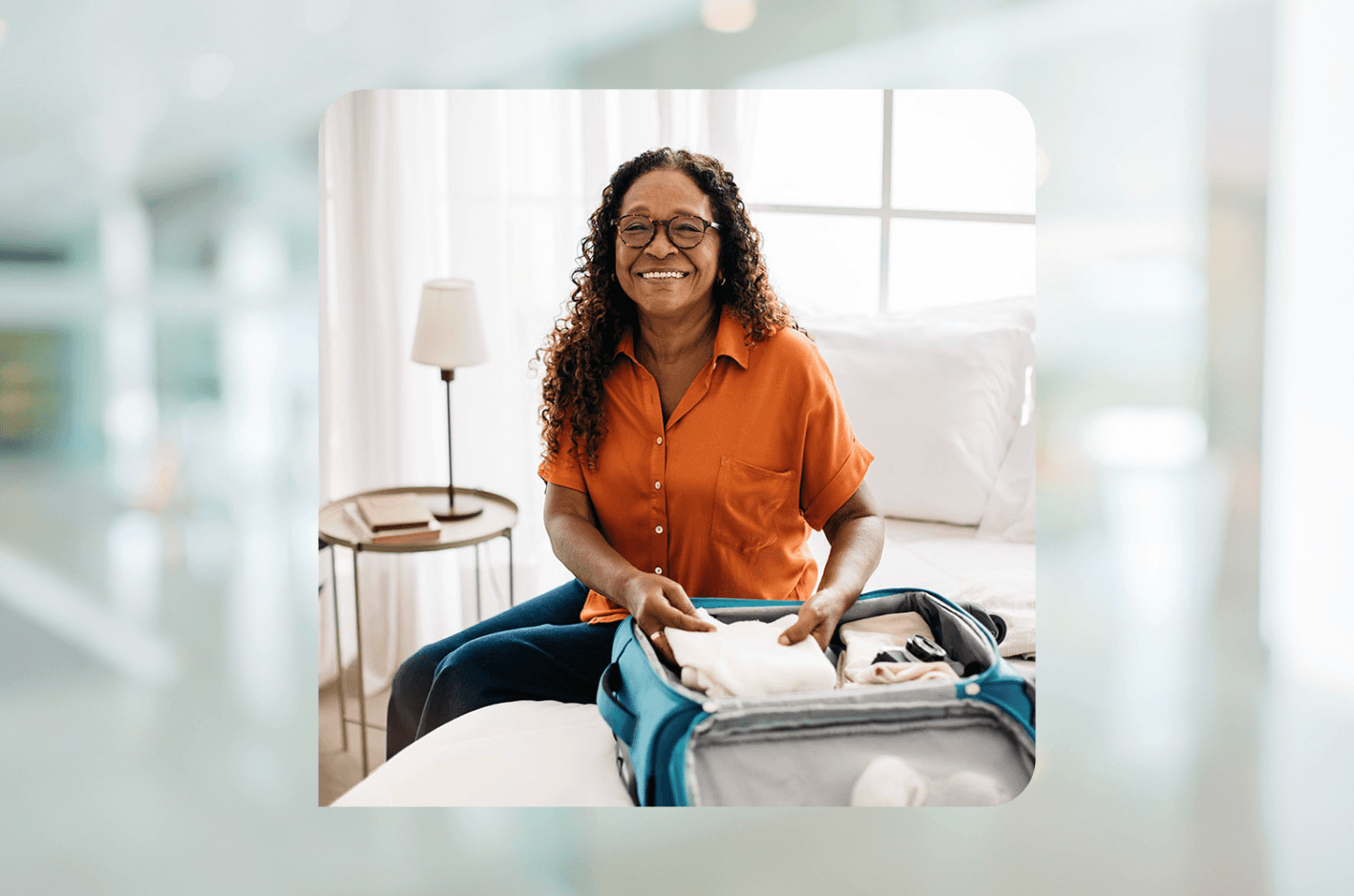 Woman smiles a the camera in a brightly lit room while packing her suitcase