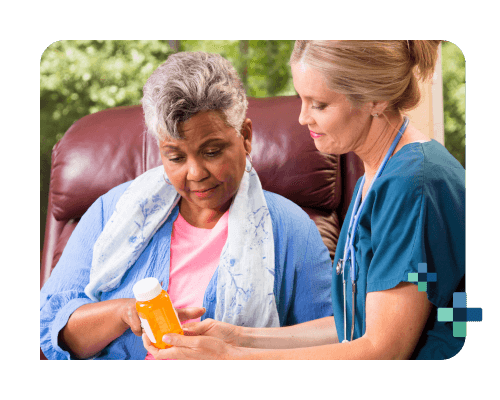 Healthcare professional in scrubs discusses medication with a seated person holding a pill bottle.