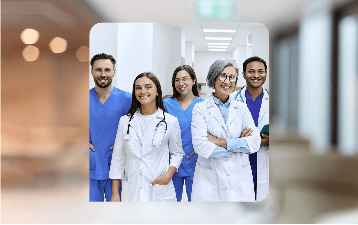 A group of healthcare professionals in scrubs and some wearing white coats smiles at the camera in a hospital hallway