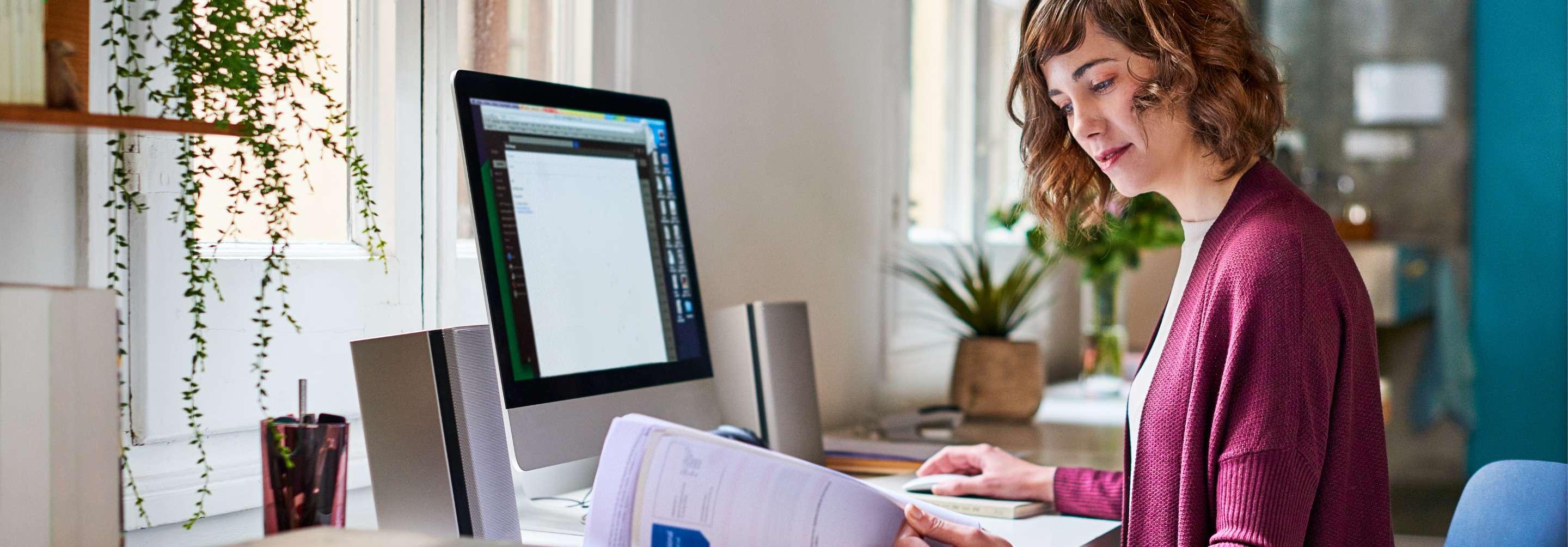A claims analyst examines papers at her desk in front of the computer