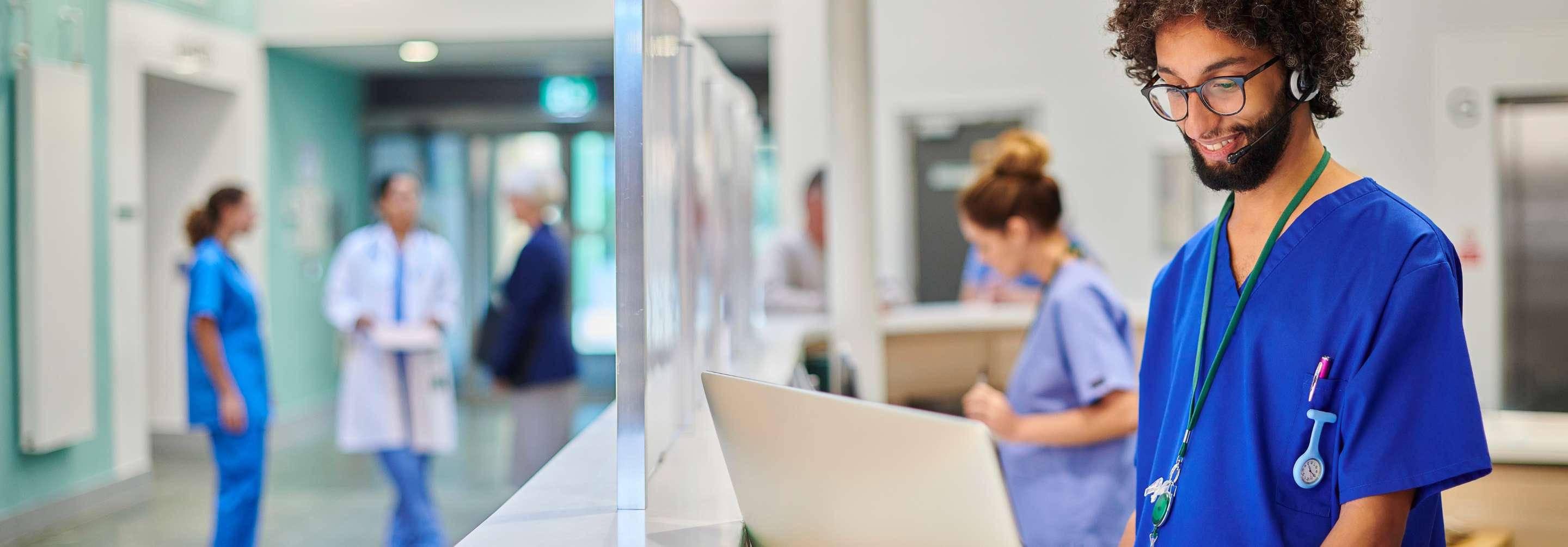 Patient care coordinator in blue scrubs smiling, looking at a computer screen in the nurses station