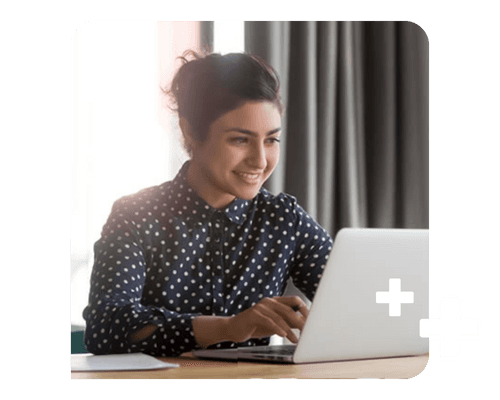 Young woman sitting at a laptop, smiling at the screen as she types