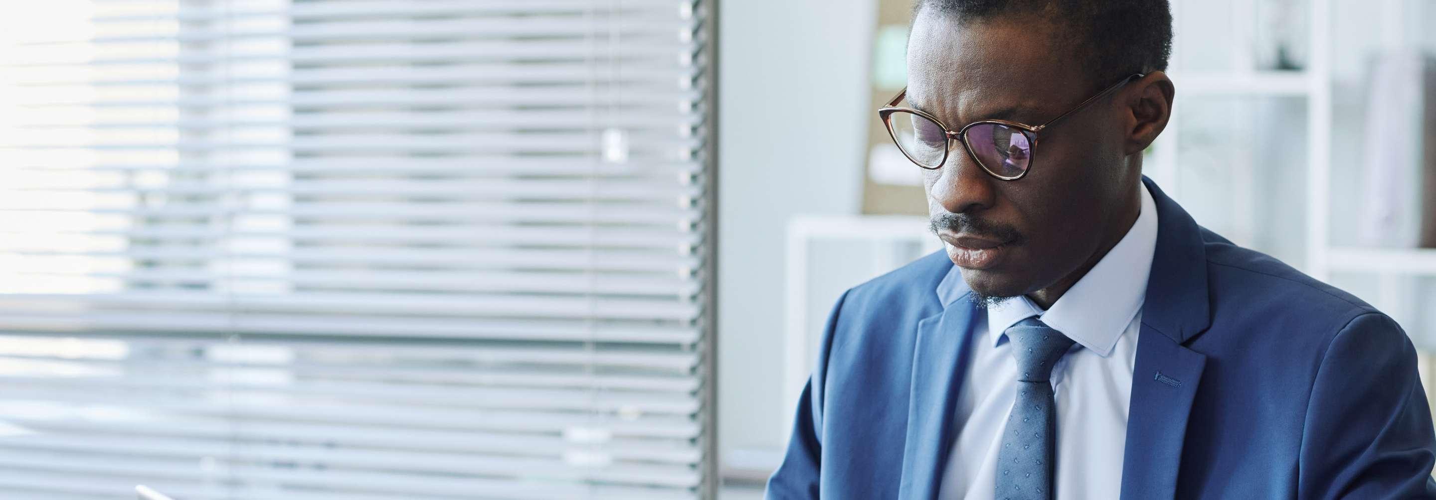 A financial analyst in a blue suit and tie sits at a meeting table, looking down