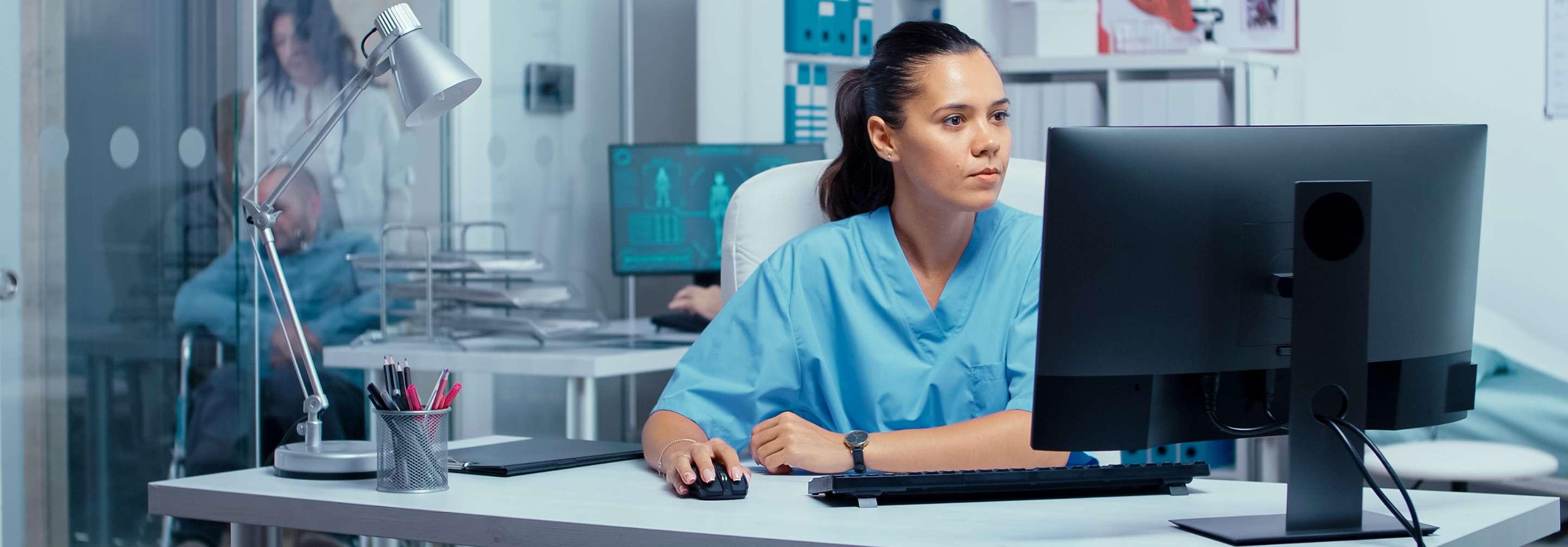 An EMR Nurse in blue scrubs looks seriously at a computer inside the hospital
