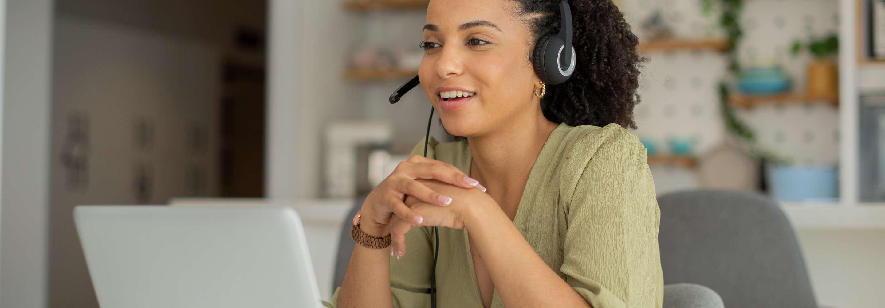 Surgery scheduler in casual close speaking to someone on the phone wearing a headset at their computer