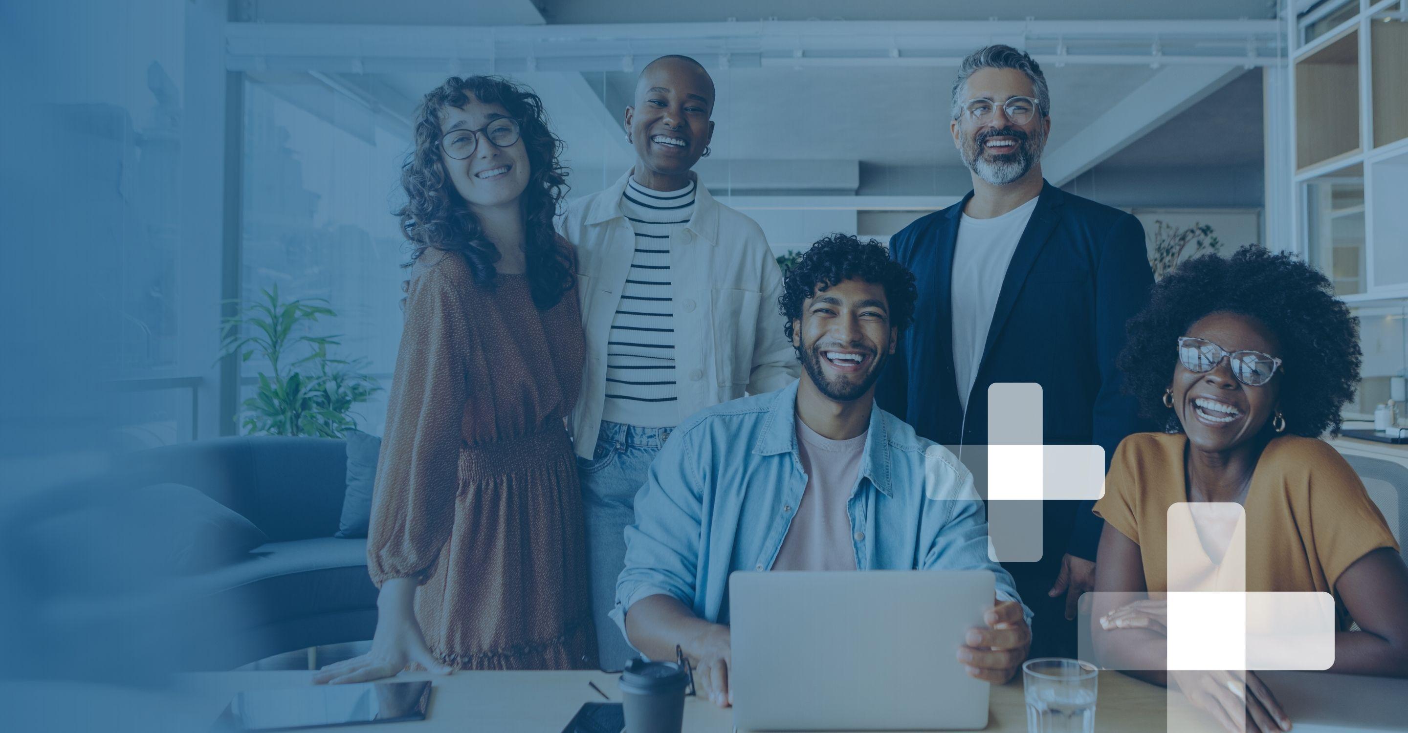 A group of professionals in business casual attire smile from around a meeting room