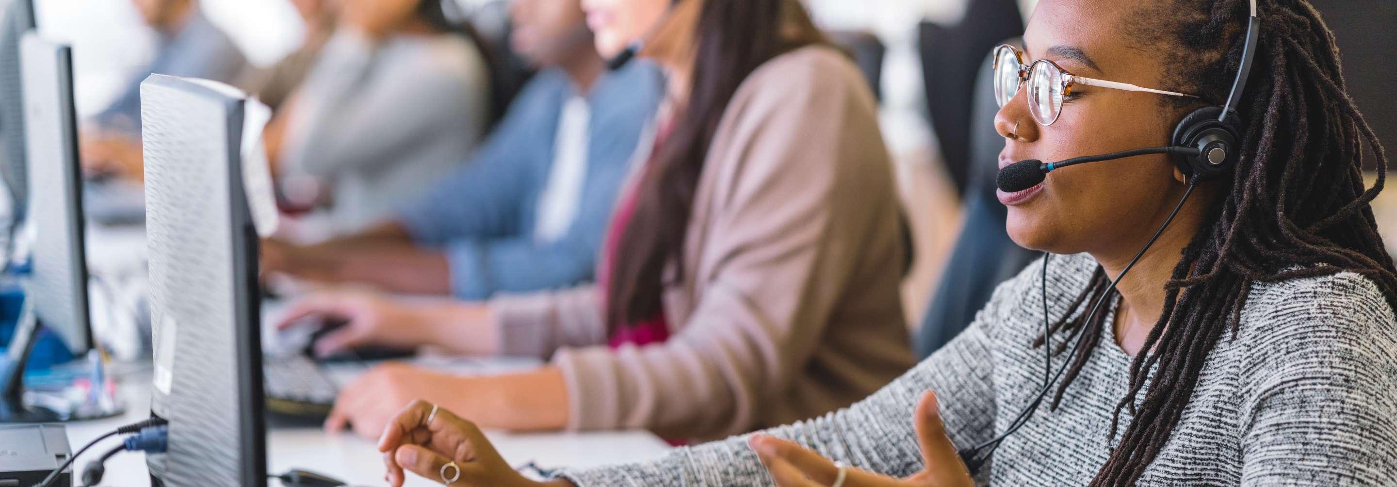 Insurance verification specialist speaking to someone over the phone on a headset while gesturing and looking at a computer screen