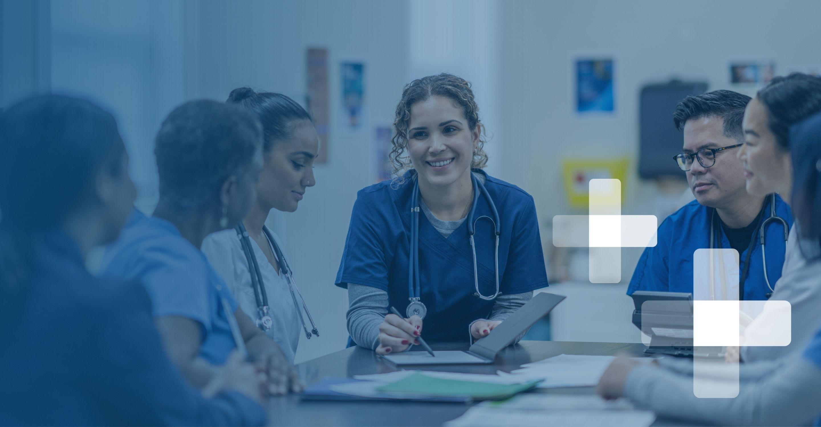 A group of healthcare professionals in scrubs sitting around a meeting table going over reports