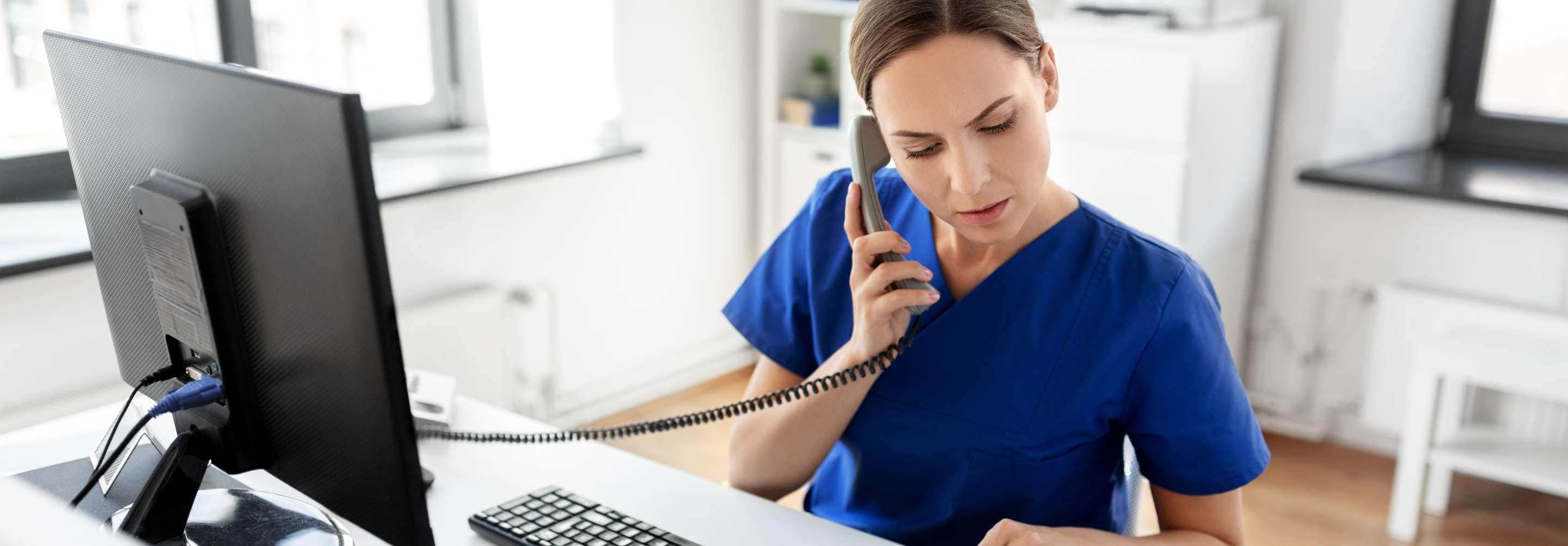 Quality improvement management in blue scrubs nurse speaking on the phone while sitting at her desk