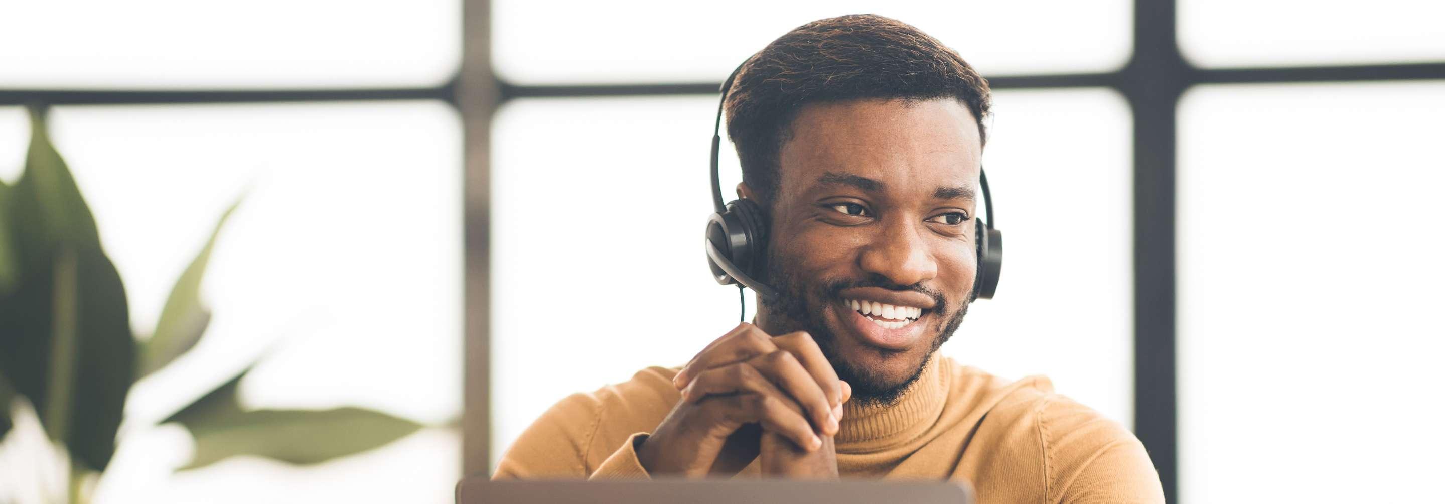 A male claims adjuster in a turtleneck speaks with someone over the phone on his headset, smiling and looking to the right