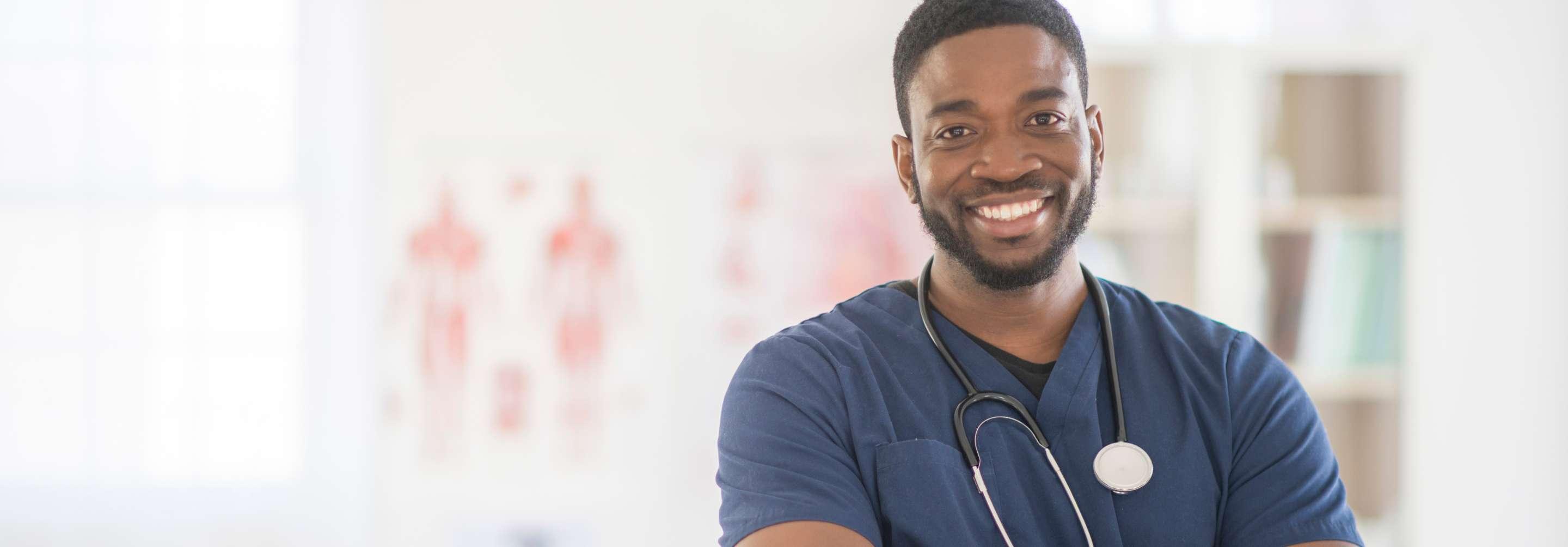 Nurse Practitioner AMP in navy blue scrubs smiling at the camera with arms crossed in a facility hallway