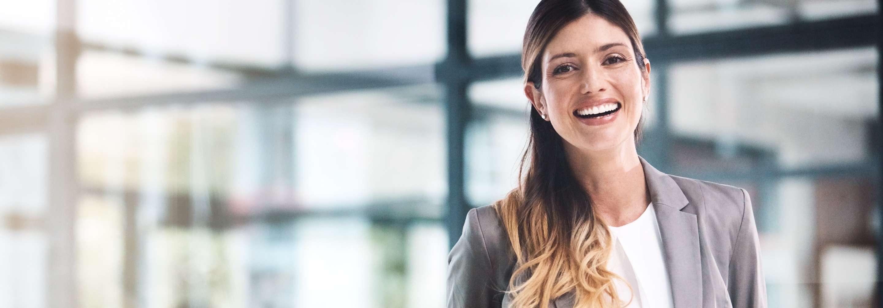 A client services specialist in a grey suit smiles widely at the camera in front of a glass corporate office lobby