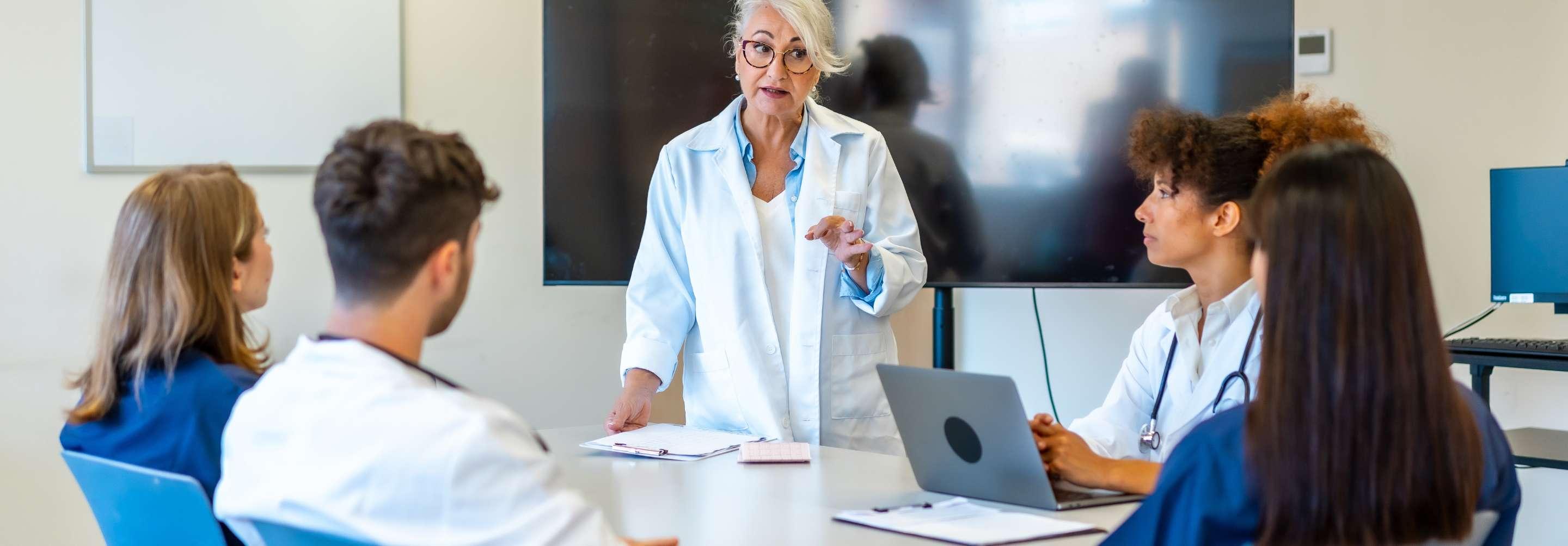 Quality improvement specialist speaking to a group wearing scrubs in a meeting room