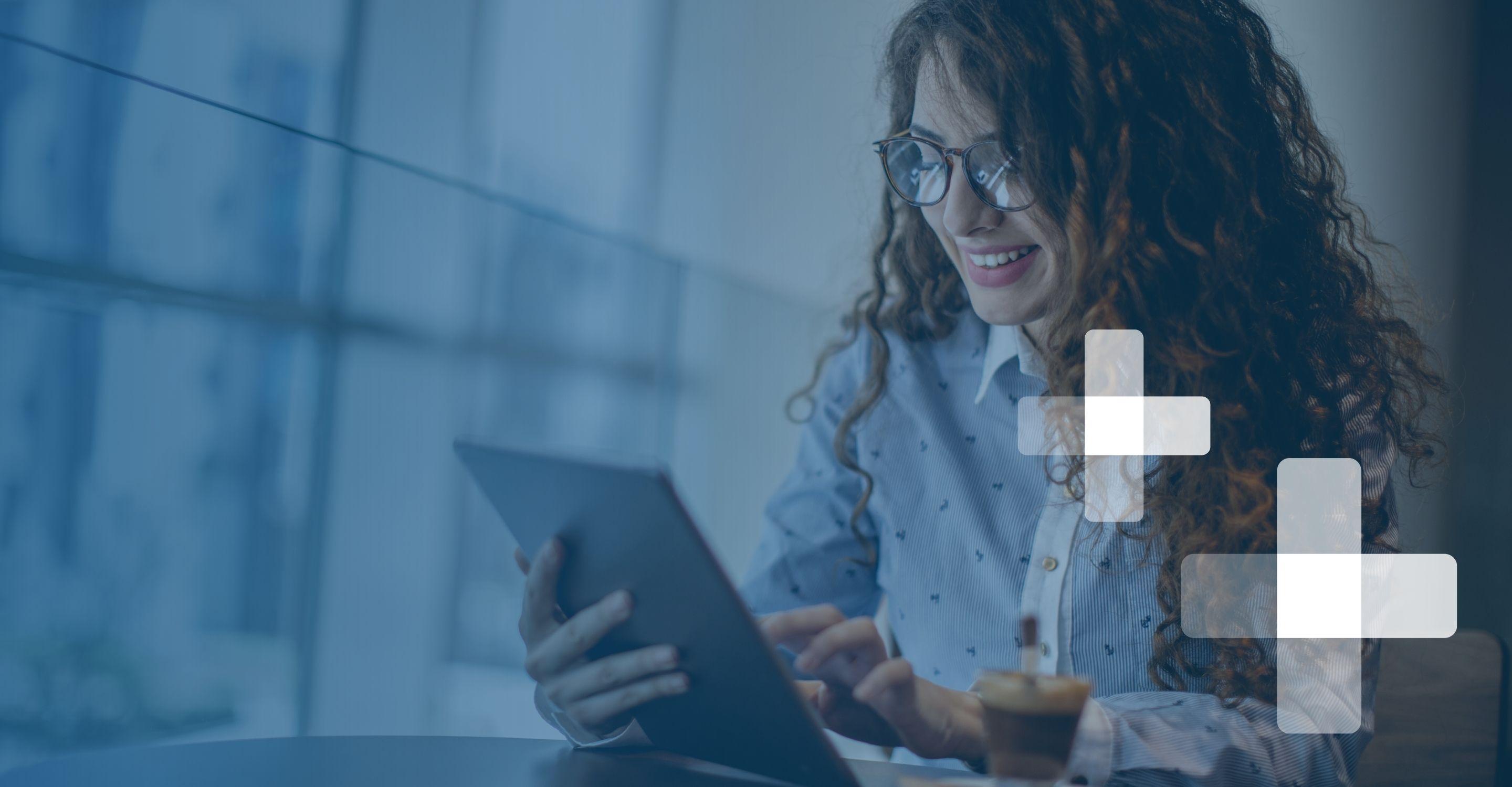 A young woman in a collared blouse smiles while using her tablet