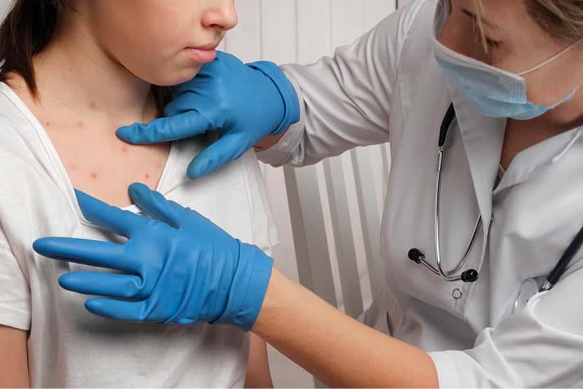 Medical professional wearing gloves examines skin rash on a patient’s upper chest.