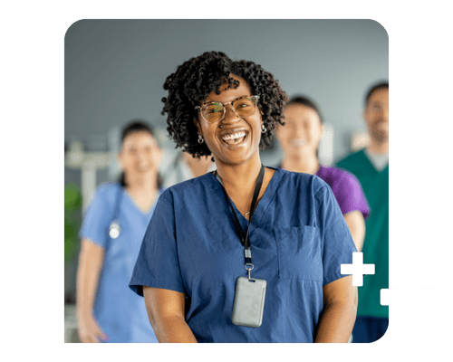 A healthcare professional in navy scrubs laughs in front of the camera; other healthcare professionals wait behind